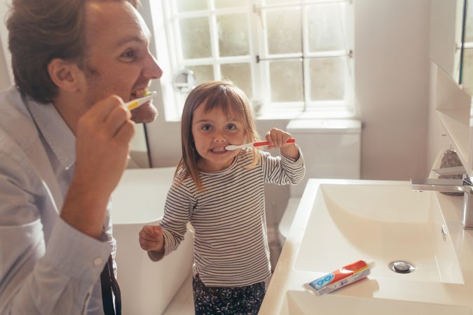 Dad and young daughter bushing teeth together