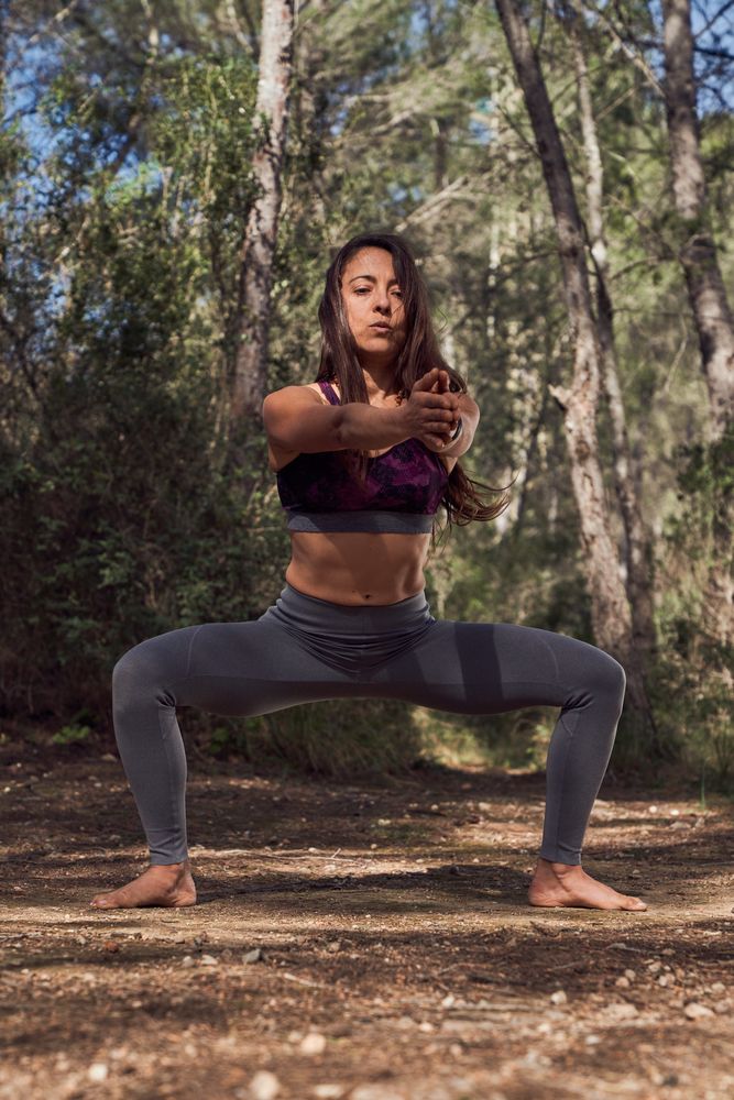 Fit woman doing plie squat for stretching in forest