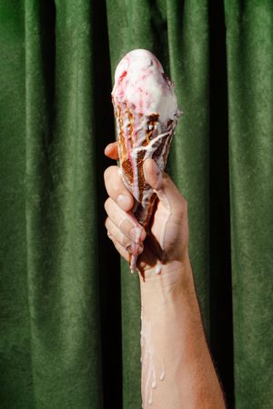 Green curtain background with hand holding melting ice cream cone