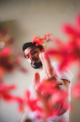 South Asian man in light shirt beside red flowers