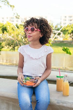 Girl with curly hair eating vegetables and fruit outdoors in a park