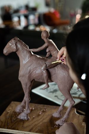 Close up of clay sculpture of horse and rider with woman’s hand