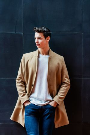 Young man leaning on dark wall outside looking away