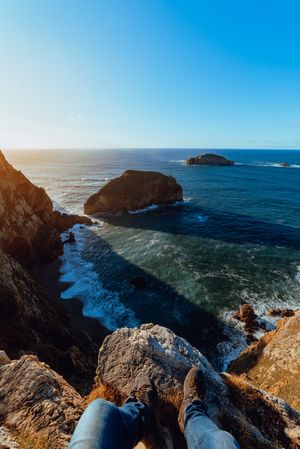 Person sitting on cliff near water
