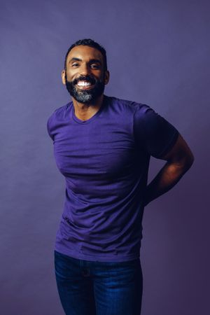 Happy male in purple studio with arms behind his back, vertical