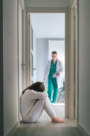 Worried physician running to help patient sitting on floor in mental health center