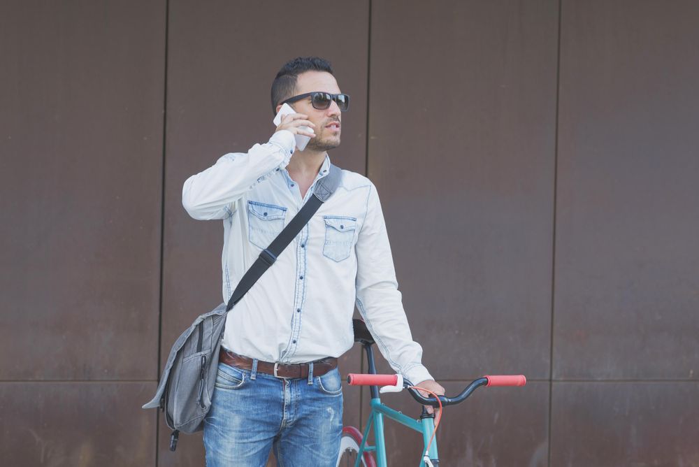 Male in sunglasses standing with red and green bicycle and looking around on phone