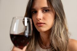 Elegant woman holding glass of red wine, thoughtful expression in dim light