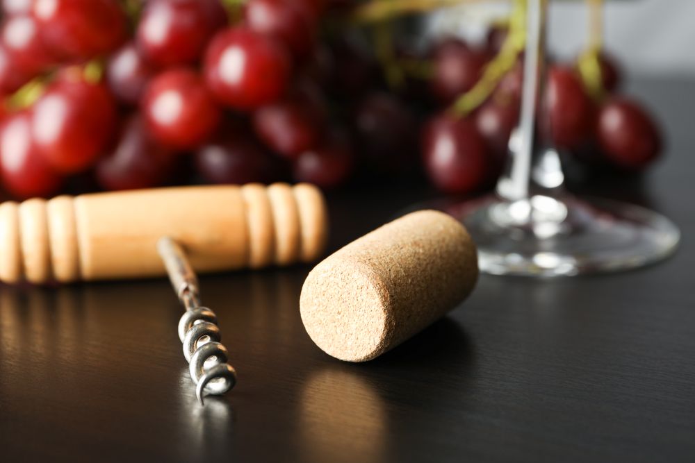 Grapes, corkscrew, cork and wine glass on dark table, close up