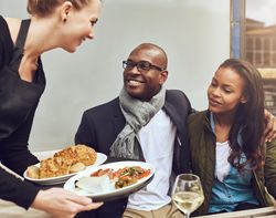 White waitress serving a smiling Black couple dining al fresco
