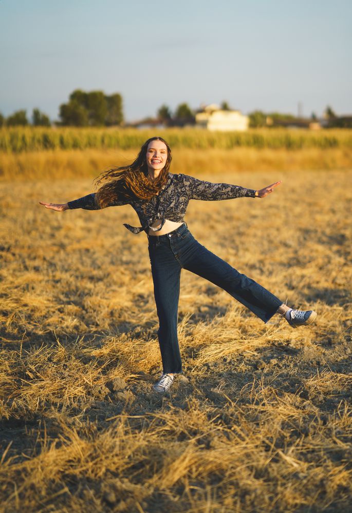 A Joyful Woman Expressively Dancing with Great Enthusiasm in a Beautiful Golden Field at Sunrise