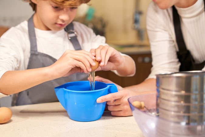 Attentive kid cooking with mom and breaking egg for dough