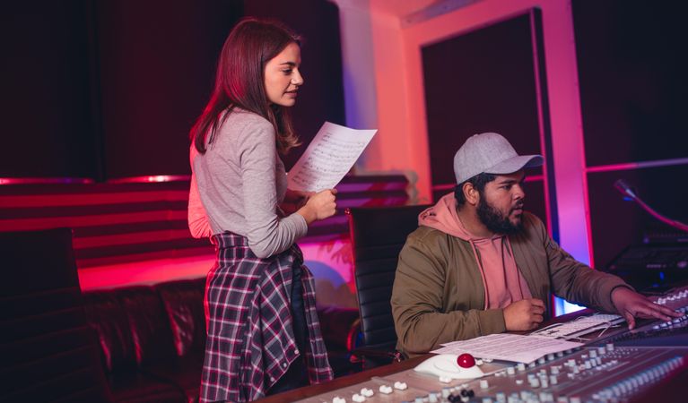Female singer with man working on audio mixing console in recording studio