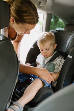 Happy mother fastening seat belts of cute kid son sitting in car seat
