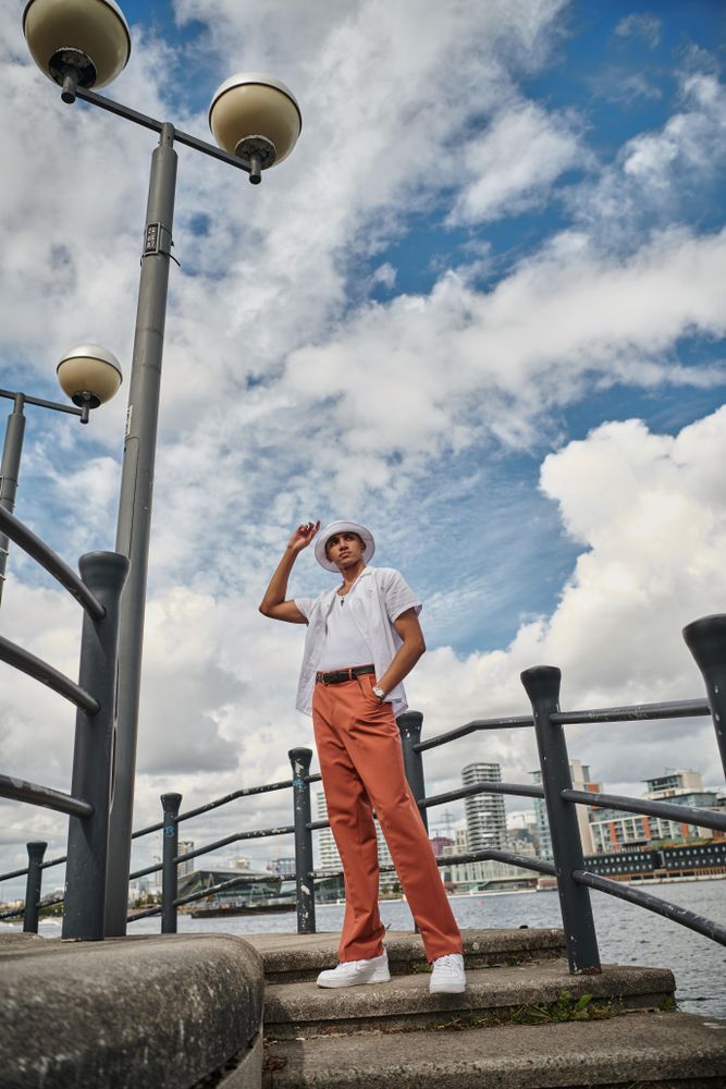 Stylish young man in hat pointing to the sky on steps by the river