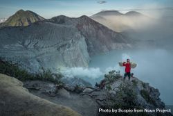 Person holding carrying pole walking near bare mountainous landform in Indonesia 5oK7y5