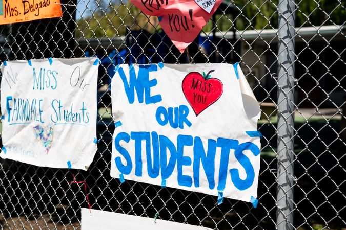 Handmade signs from teachers to students taped to a school fence during distance learning