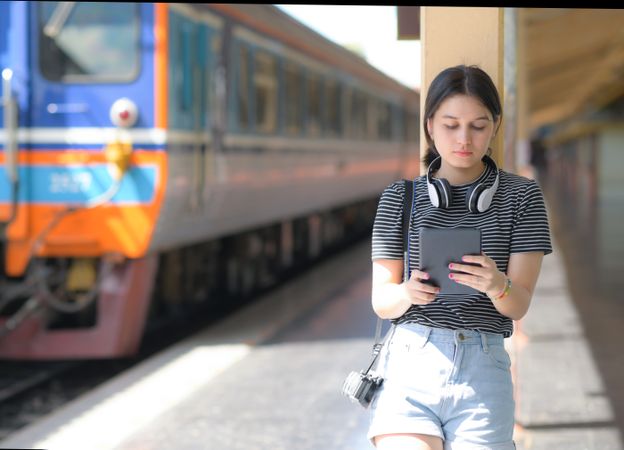 Young female traveler holding a tablet standing on a train platform