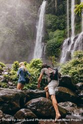 Man and woman climbing up rocks toward a waterfall 5pYwy4
