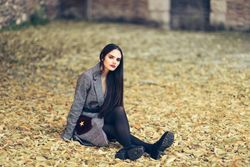 Confident female relaxing in park in fall time with colorful leaves on ground looking at camera