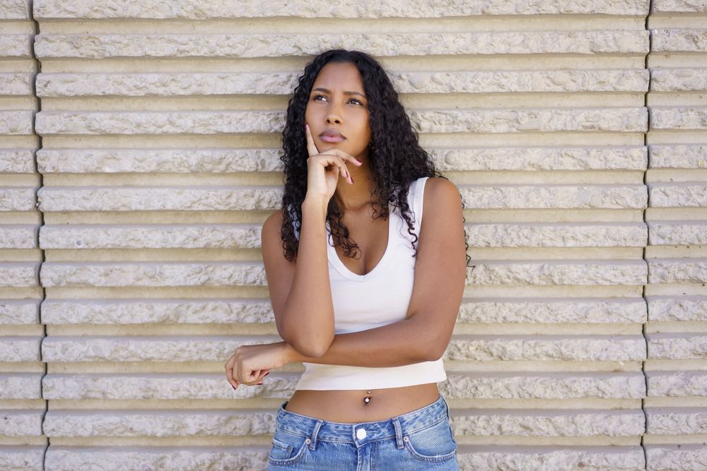 A Thoughtful Young Woman Posing Gracefully Against a Textured Wall in Natural Light