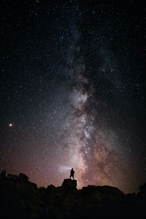 Silhouette of person standing on rock looking at the milky way