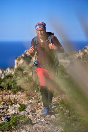 Confident male traveler walking on rocky trail in mountains