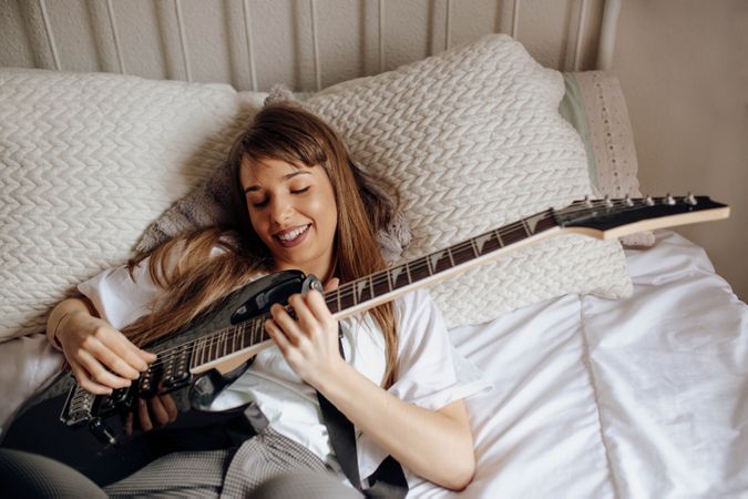 Young brunette woman playing guitar on bed