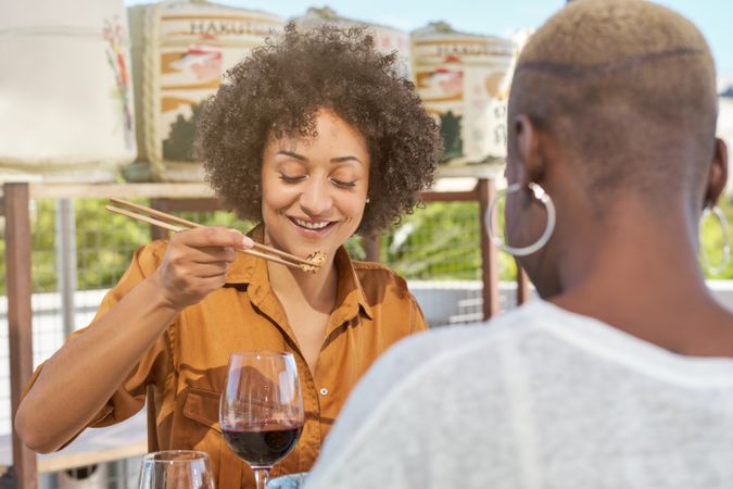 Cheerful Black female picking up fried tuna with friend in sushi