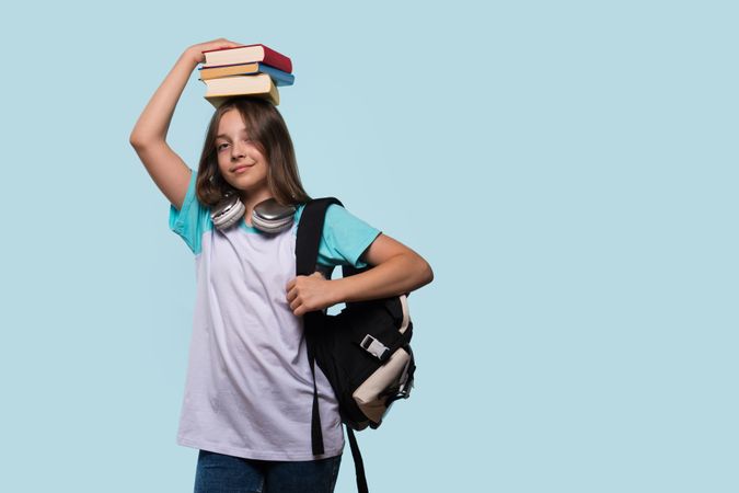 Girl balancing books on head, wearing backpack and headphones