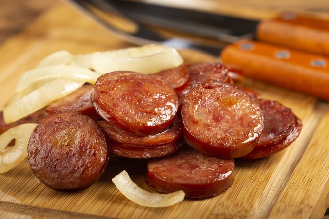 Sliced calabrese sausage with onion on wooden background.