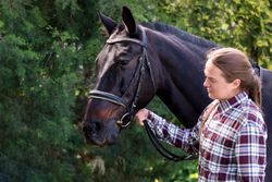 Woman holding a bridled horse outdoors.