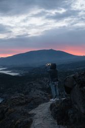 Male taking photo with smartphone on cliff at dusk