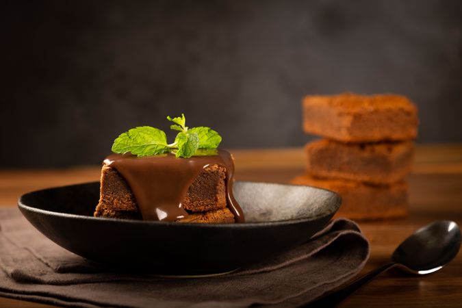 Side view of chocolate brownies served on wooden board with pot of syrup on the side