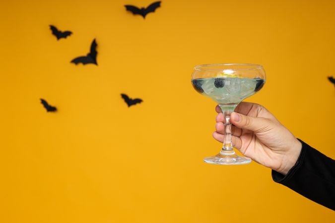 Cocktail in hand, on a yellow background with bats