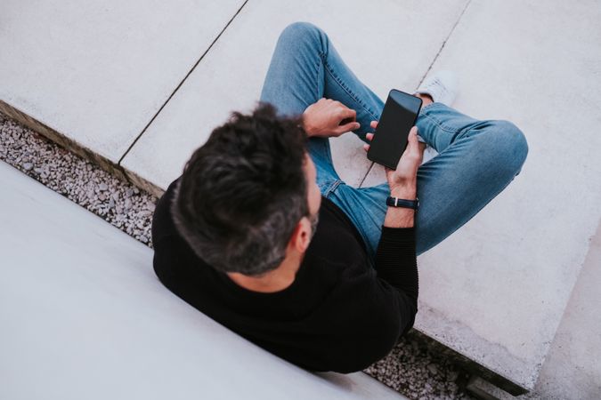 Adult stylish smiling man using a smartphone near grey wall