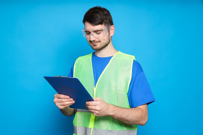 Young man civil engineer with clipboard on blue background