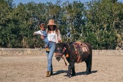 Young mother carrying child while walking in paddock with purebr