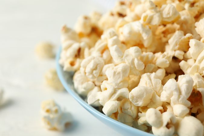 Plate with popcorn on light background, space for text