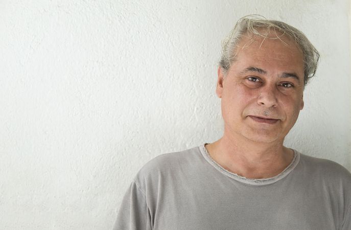 Portrait of smiling middle aged man in gray shirt against light background