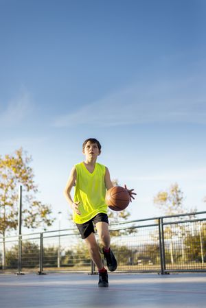 Boy in yellow shirt plays basketball on city playground