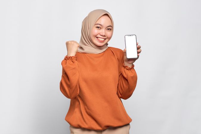 Muslim woman smiling while holding up smart phone mock up screen looking happy