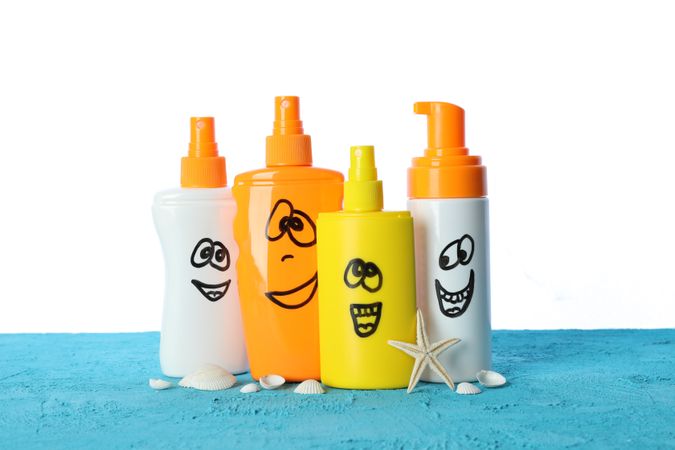 Happy sunscreen sprays with starfish and seashells on color table isolated on blank background. Safe tan