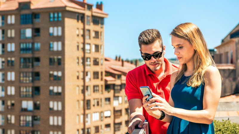 Young couple looking mobile in rooftop on a summer day
