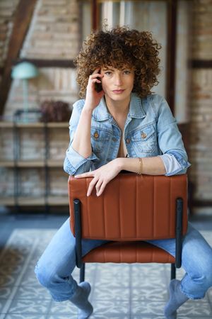 Woman with curly hair sitting on chair reversed with hand in hair