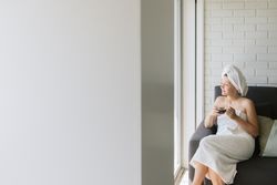 Adult relaxed woman enjoying life while resting on sofa and having hot drink after shower in own cozy apartment