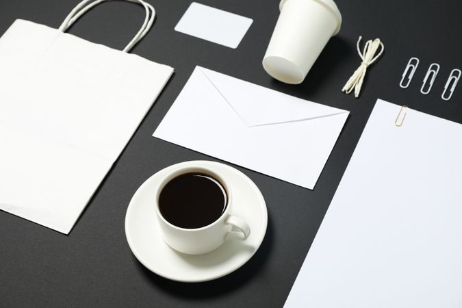 Blank stationery, paper bag and cup of coffee on dark background. Mockup