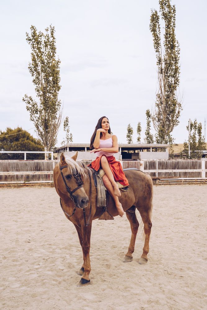 Graceful rider sitting at harnessed horse walking along paddock