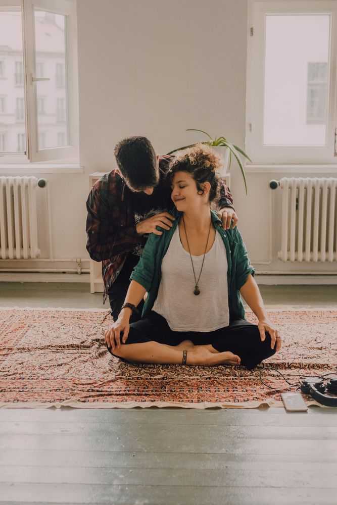 Man rubbing shoulders of joyful woman resting on floor at home