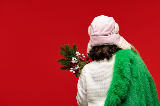 Woman in winter hat and green coat holding festive bouquet.